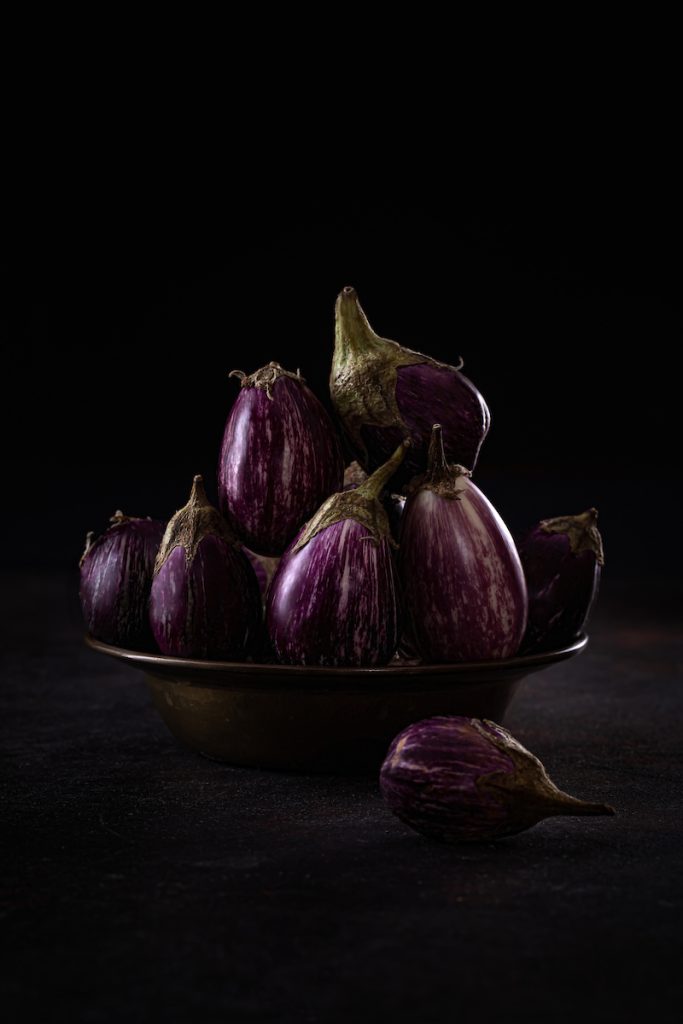 Mini melanzane in ciotola su sfondo scuro, still life.