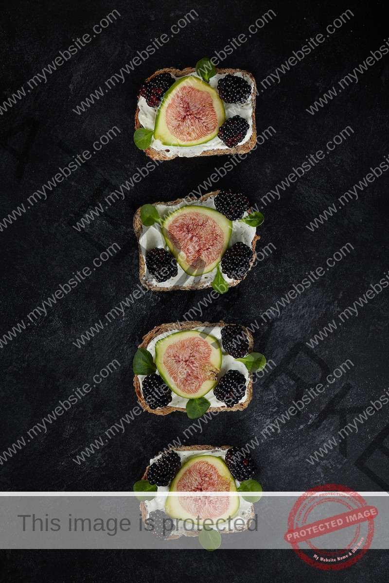 Bread with spreadable cheese, figs, blackberries and lamb's lettuce on a dark background.