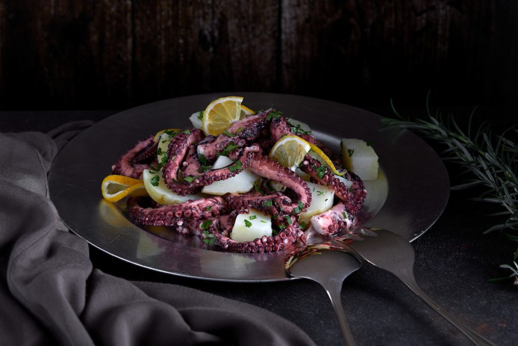 Insalata di polpo e patate con limone su piatto scuro.